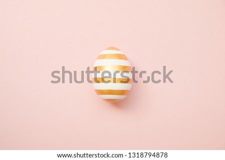 Easter golden with striped patternd egg on pastel pink background. Minimal easter concept. Happy Easter card with copy space for text. Top view, flatlay.  