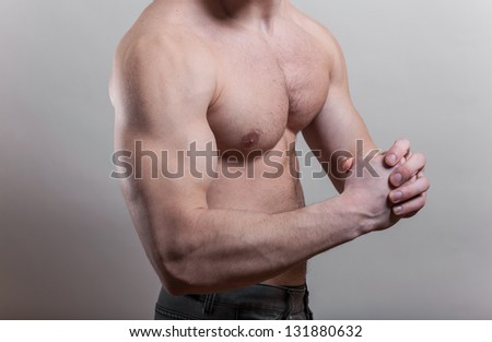 Flexed biceps. Very strong young guy over gray background in studio.