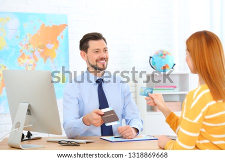 Male manager giving passport with ticket to client in travel agency