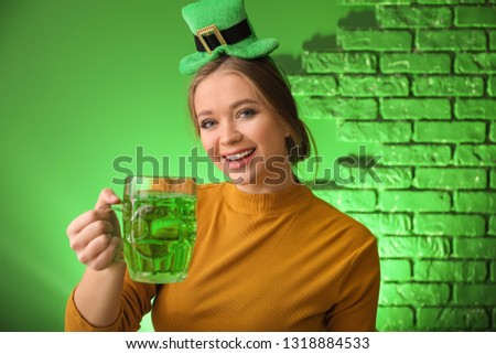 Beautiful young woman with green hat and mug of beer on color background. St. Patrick's Day celebration