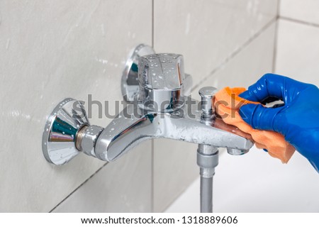 Close-up of the shower faucet and showerhead cleaning process from lime scale, white chalk sediment and stains using a commercial soap scum remover. Bathroom cleaning and disinfection Royalty-Free Stock Photo #1318889606