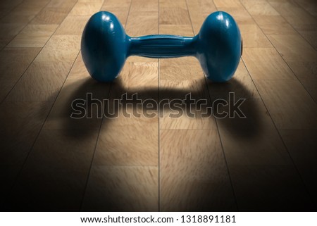 Close-up of an old blue dumbbell for weight training or fitness on a parquet wooden floor of the gym