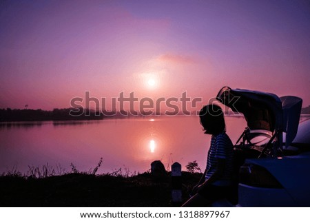 Teen girls sitting behind the car watching the sunrise on holidays.