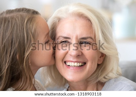 Cute little grandchild kissing excited grandmother on cheek, laughing grandma enjoying care of grandchild congratulate with mothers day, showing support and love, warm family relations close up