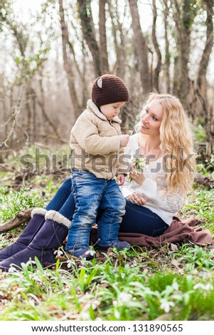 Smiling mother and little son on grass and snowdrops in park