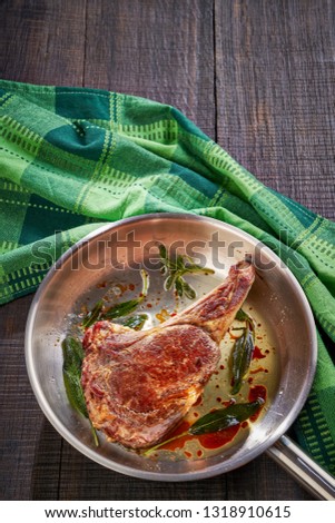 Close up on australian gourmet tomahawk rib beef steak in a skillet with fried sage with green kitchen dish towel on a dark wooden background, vertical