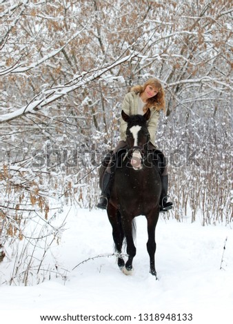 Pretty woman riding her horse through snow woods