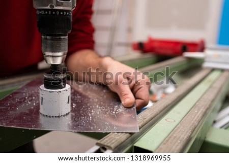 worker cutting a hole on aluminium plate with a crown drill Royalty-Free Stock Photo #1318969955