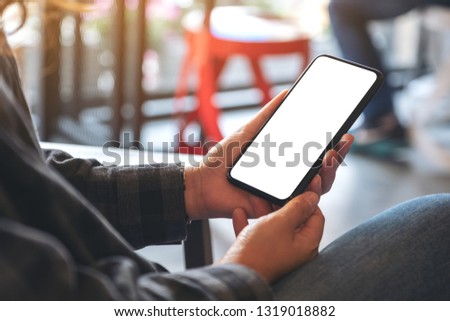 Mockup image of hands holding black mobile phone with blank white desktop screen in cafe