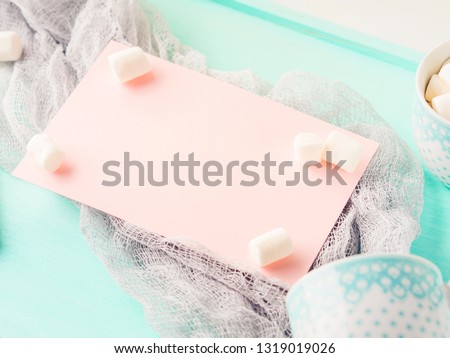 Pink card and marshmallows on turquoise background with envelope and coffee cups. Pastel colors