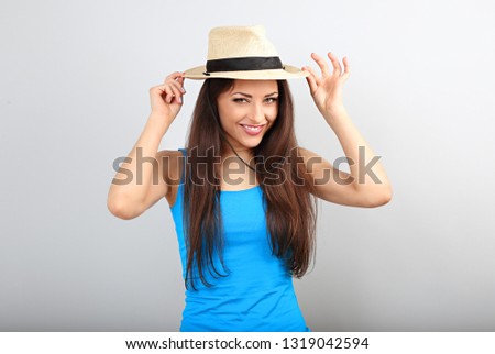 Friendly casual calm woman in blue top holding straw hat and looking happy with long volume hairstyle on blue color copy space background