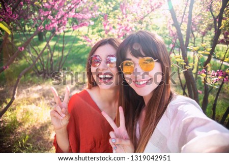 Image of young happy women friends standing in blossom spring park. Looking at camera make selfie. 