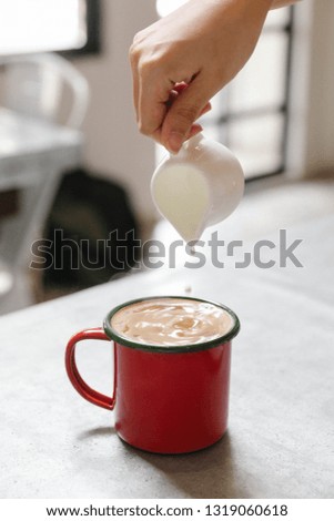 Fresh milk pouring in hot coffee in red cup that see the milk drops with steam.