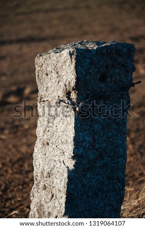 Rustic countryside granite stone vertical boundary fence post limit with barb wire on an agriculture field landscape during spring sunset in Spain 