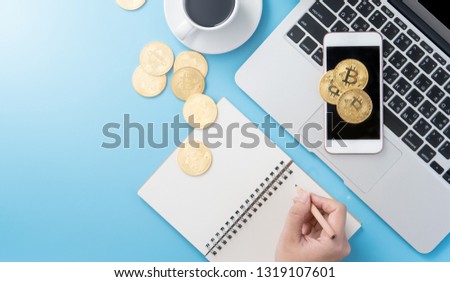 A woman is accounting the money concept isolated on clean blue office working desk with bitcoin and coffee cup, workspace design, mock up, top view, flat lay, copy space, close up