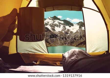Thermos cup in hand. Stay in tent in nature. concept of Hiking and life in the wild. Good morning overlooking the beautiful mountains.