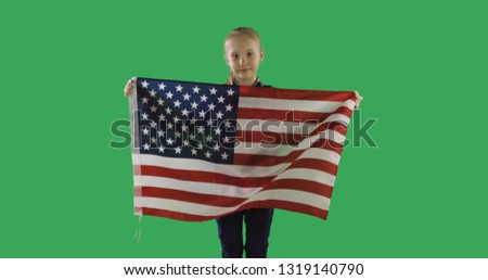 Cute girl holding American flag with pole, stars and stripe on chroma key green screen. USA flag fluttering in the wind.