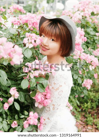 Beautiful young brunette woman in white lace dress and hat posing in rose garden. Outdoor fashion portrait of glamour Chinese stylish girl. Emotions, people, beauty and lifestyle concept.