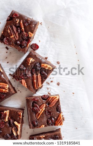 
homemade chocolate fudge brownies with pecan nut and dried cranberry on white baking paper background