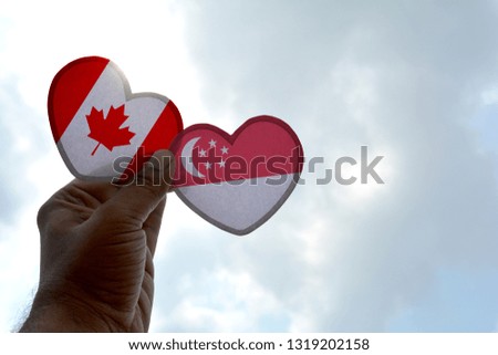 Hand holds a heart Shape Canada and Singapore flag, love between two countries