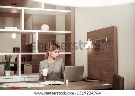 Finishing work. Young appealing blonde-haired woman finishing her work and drinking some tea