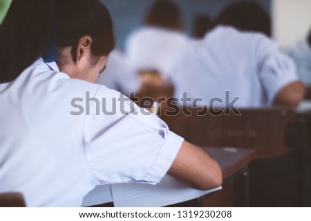 School student is taking exam and writing answer in classroom for education test concept.