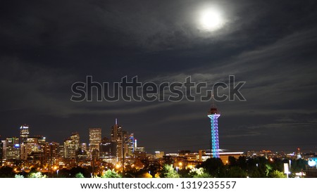 Downtown Denver at night with a full moon over the skyline.  This photo shows the full moon rising into the night sky above the Denver Colorado skyline. 