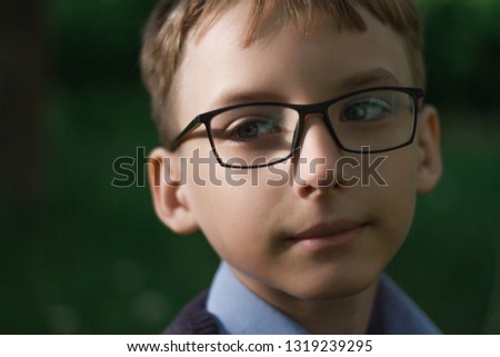 A boy with glasses in a blue shirt is sitting in the grass