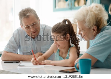 Little lady drawing a picture with grandma and grandad. Family's hapiness, fun time and being together.