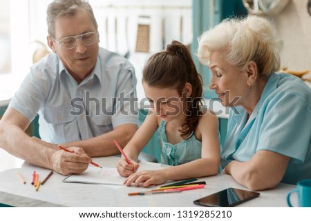 Little girl and her grandparents drawing a picture. Spending time together with fun and entertainment.