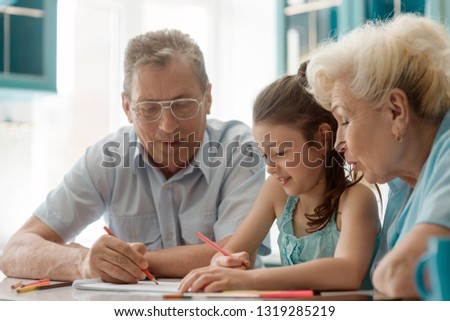 Girl and grandparents drawing a picture for a school project. Family's support and fun time spent together.