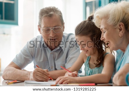 Kid and grandparents having fun while drawing with color pencils. Family, warm atmosphere and great memories.