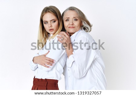 Cute elderly woman hugging her granddaughter in white shirts on a light background Family