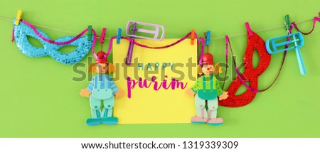 Purim celebration concept (jewish carnival holiday) with note, clown and noisemaker over wooden green background