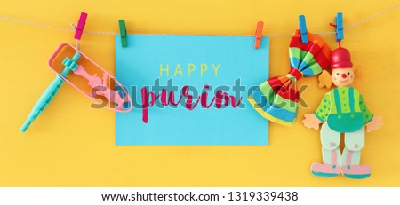 Purim celebration concept (jewish carnival holiday) with note, clown and noisemaker over wooden yellow background
