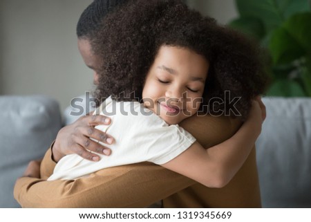 Cute funny mixed race child daughter embracing black father holding tight feeling love connection affection concept, happy african family dad and little kid girl hugging cuddling bonding at home Royalty-Free Stock Photo #1319345669