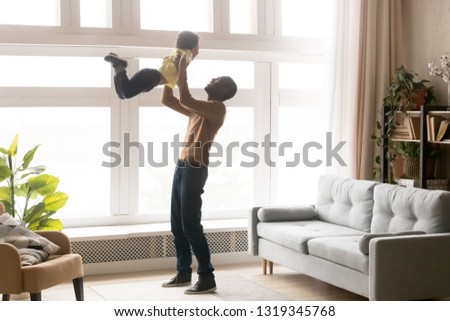 Happy african dad lifting little toddler son up playing at home, loving black dad holding kid boy having fun in modern living room together, small child enjoying weekend activity time with father Royalty-Free Stock Photo #1319345768
