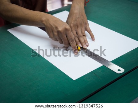 Close-up hands cutting white paper with cutter and iron ruler on green mat