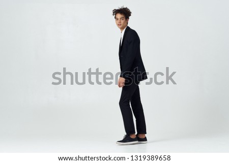 Cute curly guy in a black suit is standing on a gray background office worker