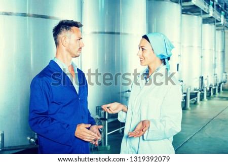 Two young winery workers in protective uniform talking in secondary fermentation section
