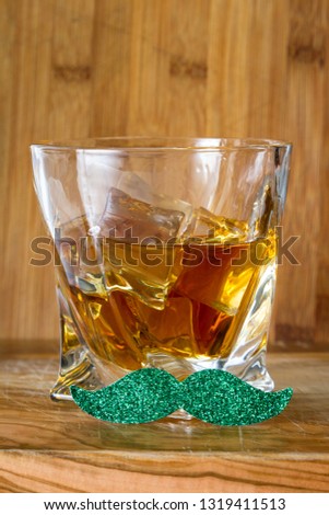 Close up fo a glass of whiskey with a green mustache over a wooden background as a concept for Saint Patricks day