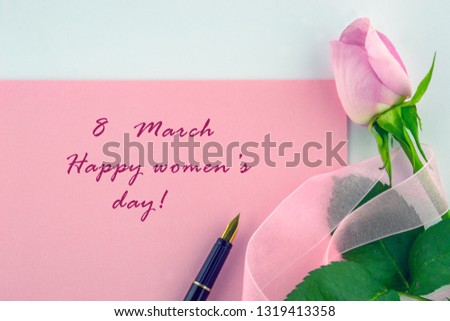 International Women`s Day, March 8. The happy woman`s day is a sign of greeting, pink rose wrapped in a decorative pink ribbon and pen on a white background.