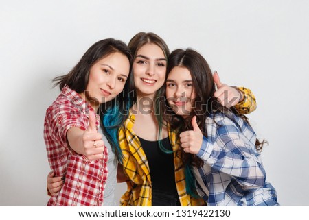Portrait of three beautiful young happy females smiling joyfully showing thumbs up on white background