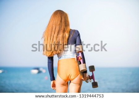 Close up of beautiful young woman in swimsuit holding skateboard deck in hands, back view