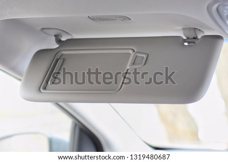 Car visor. Car interior. Grey open sun car visor with selective focus and car mirror on blurred background with automobile window Royalty-Free Stock Photo #1319480687