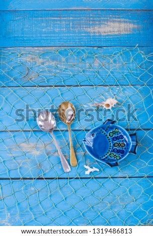 fishing net on a blue wooden background, plate - fish, shells, old seashell spoons. Free space for text.