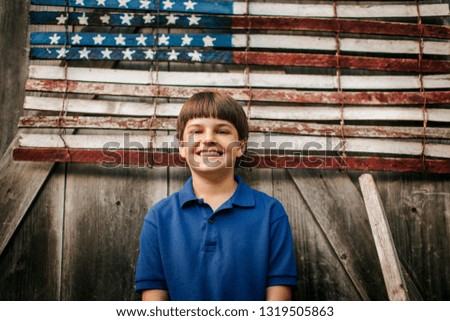 Portrait of a smiling young boy standing in front of an American flag.