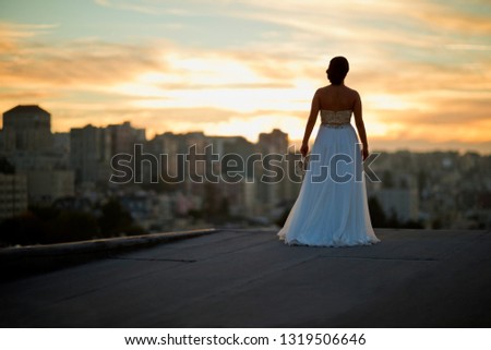 Young bride watching the sunset over an urban skyline.