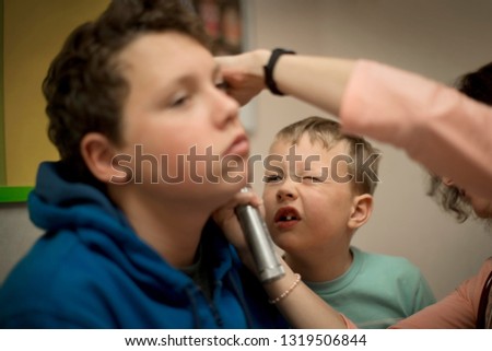 Young boy looking into his brother's ear as it is examined by a female doctor.