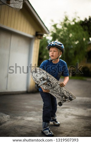 Young boy holding his skateboard while standing on a residential driveway.